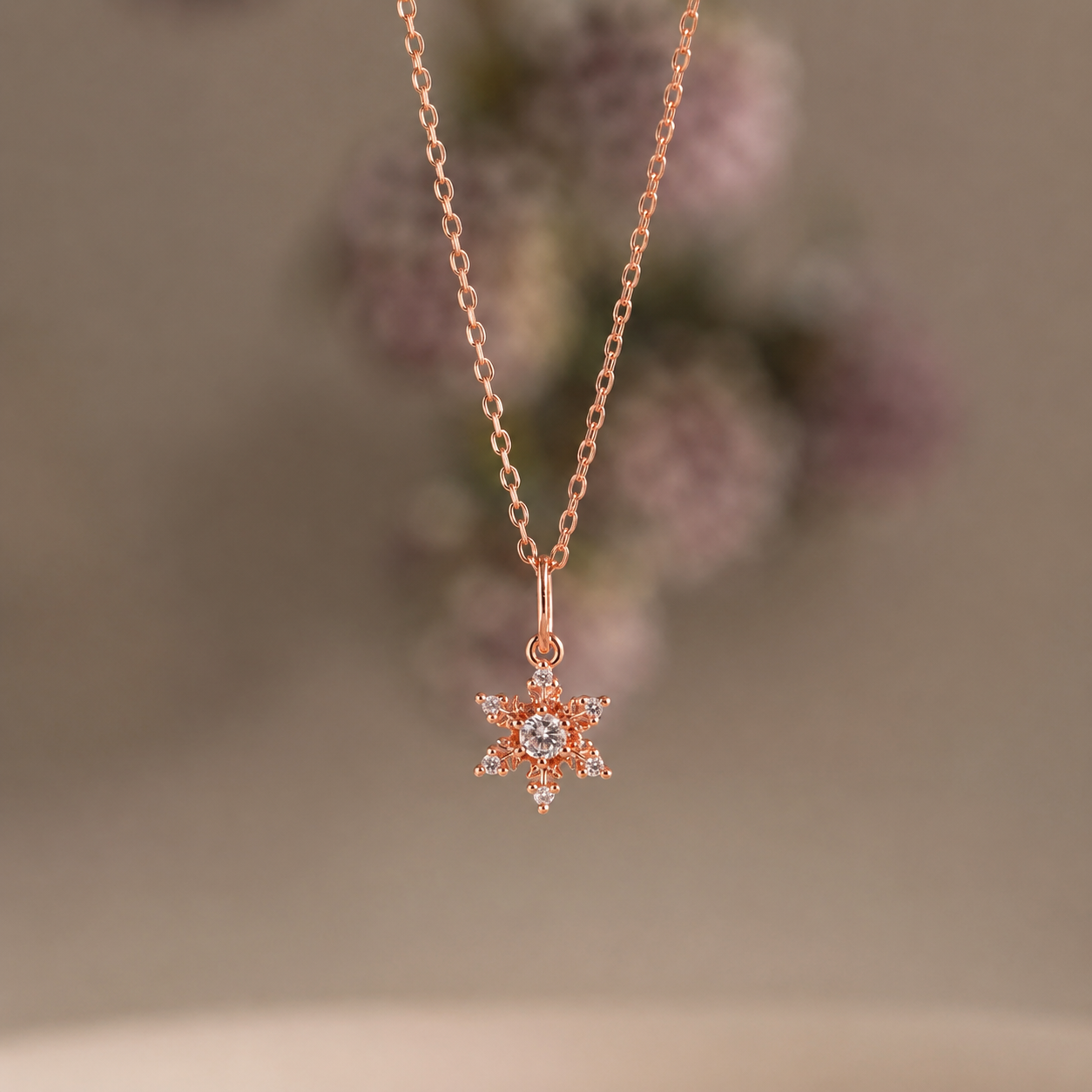 Rose gold necklace with a snowflake pendant on a blurred floral background